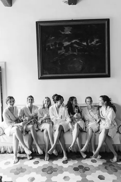 Bridesmaids and bride relaxing barefoot on a sofa with champagne flutes, sharing laughter inside Villa Ravano.