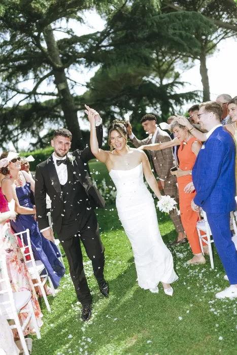 Bride and groom exit the ceremony hand in hand as guests toss petals at Villa Ravano.