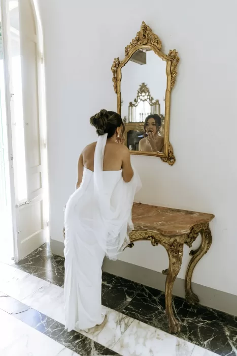Bride touching up her makeup in an ornate gold mirror moments before the ceremony at Villa Ravano.