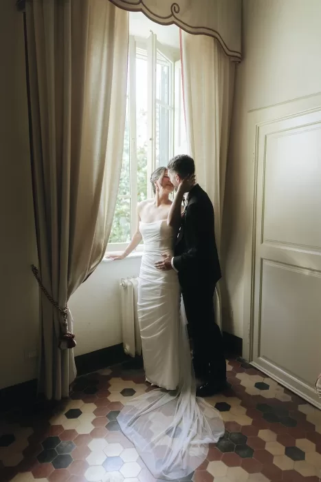Bride and groom share a tender moment by the window, bathed in soft light inside Villa Ravano.
