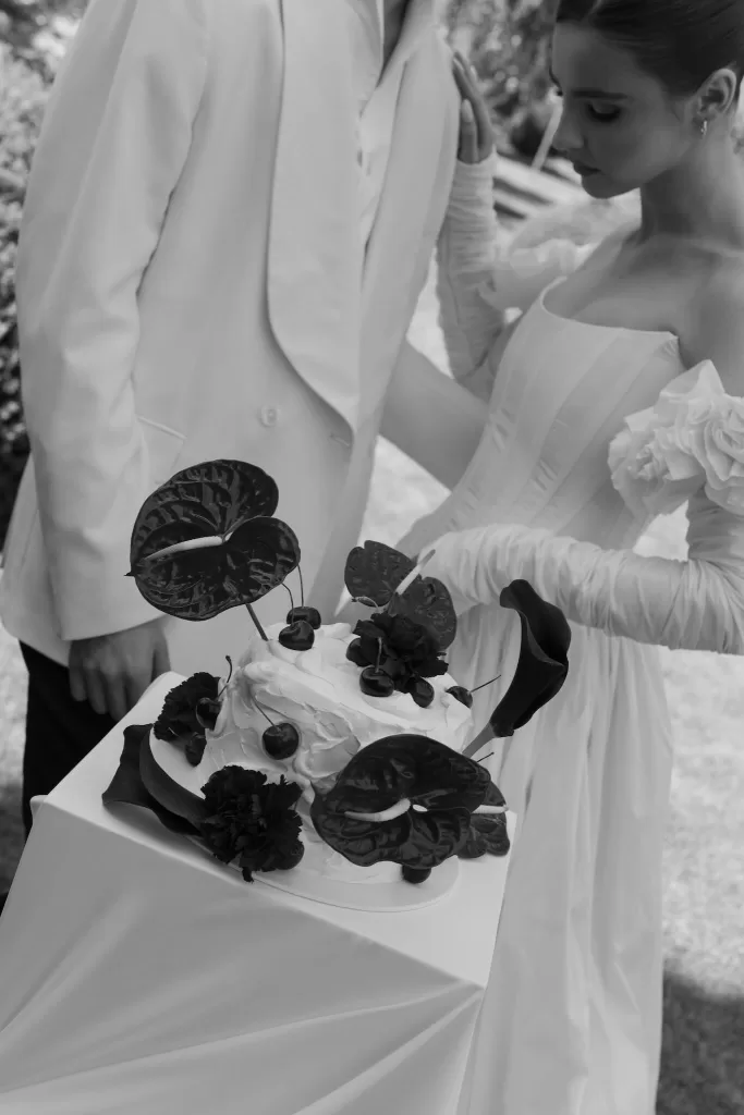 Couple admiring an artistic wedding cake adorned with cherries and dark tropical flowers at Treelove Parkas.