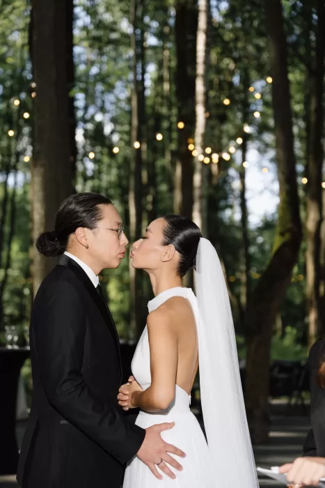 Bride and groom leaning in for a kiss under string lights in forest wedding setting