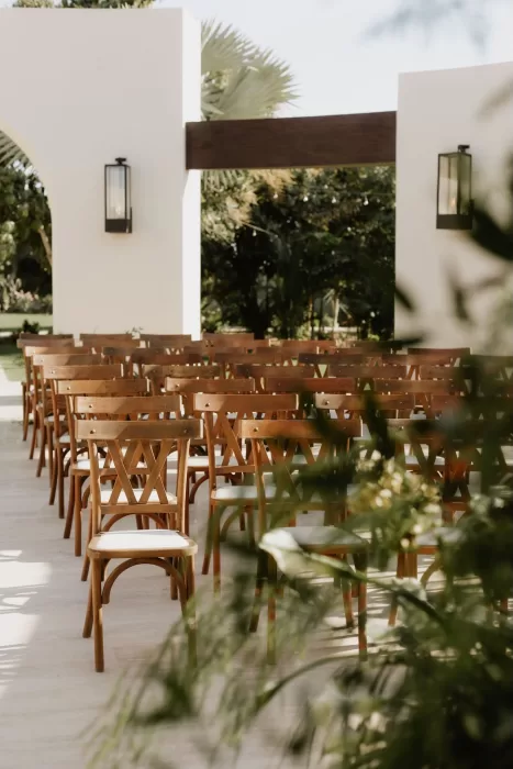 Rows of wooden ceremony chairs at Baja Luna with greenery and modern white walls.