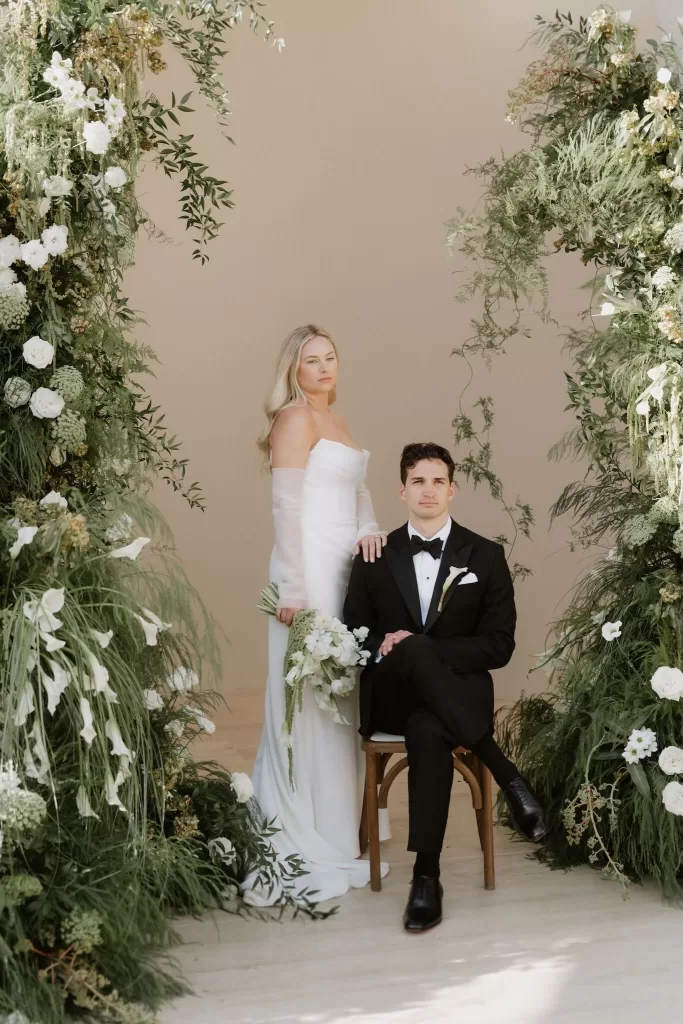 Bride and groom posing beneath lush floral ceremony arch at Baja Luna.