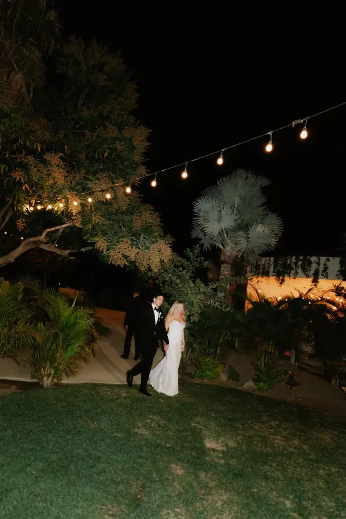 Bride and groom walking hand in hand at night under string lights at Baja Luna.