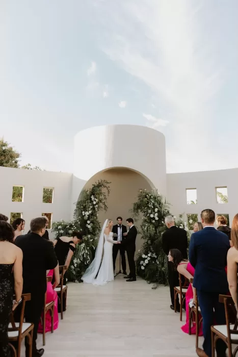 Bride and groom exchanging vows under a round archway adorned with greenery at Baja Luna.