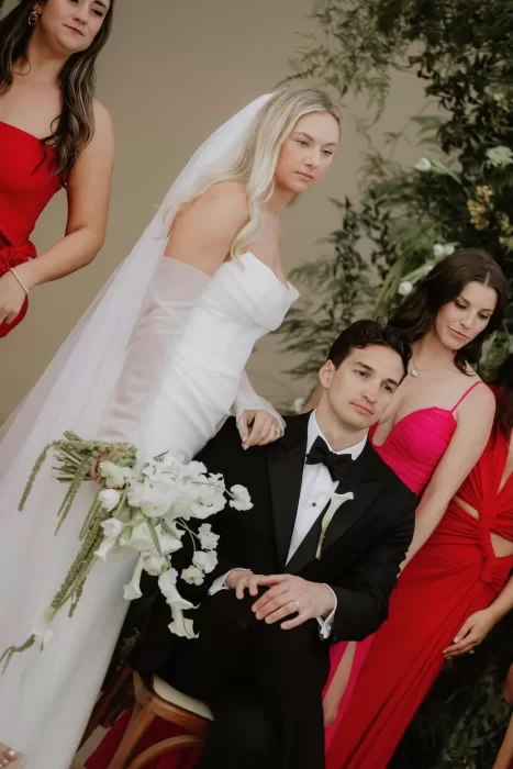Bride and groom with wedding party in pink and red dresses at Baja Luna ceremony arch.