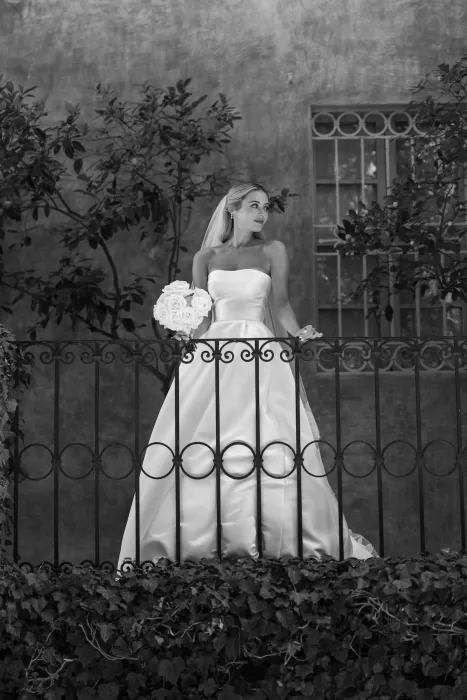 Bride holding a bouquet of roses on a wrought-iron balcony at Borgo Stomenanno, in soft black-and-white.