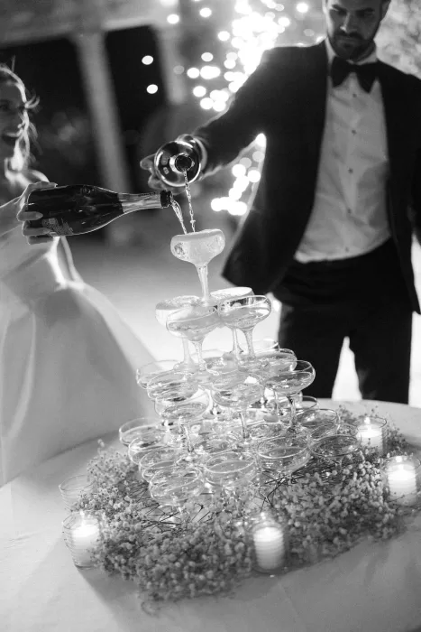 Bride and groom pour champagne together under fairy lights at their Borgo Stomenanno celebration.