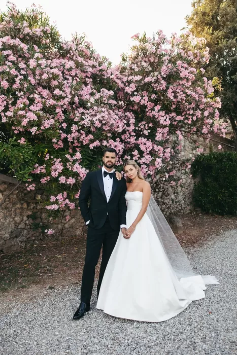 The bride and groom stand in front of lush pink blossoms at Borgo Stomenanno.