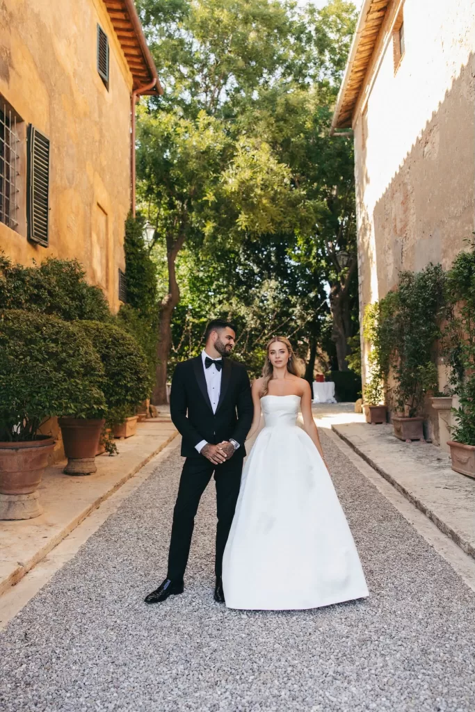 Bride and groom standing in the sun-dappled courtyard of Borgo Stomenanno, surrounded by Tuscan charm.