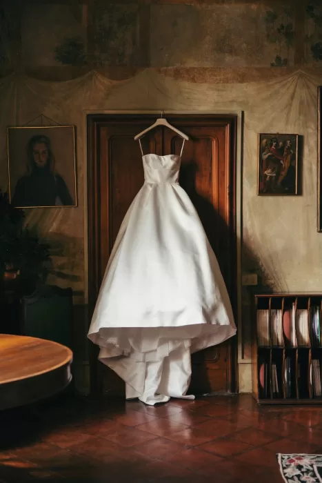 A classic white wedding dress hangs elegantly in a vintage room at Borgo Stomenanno.