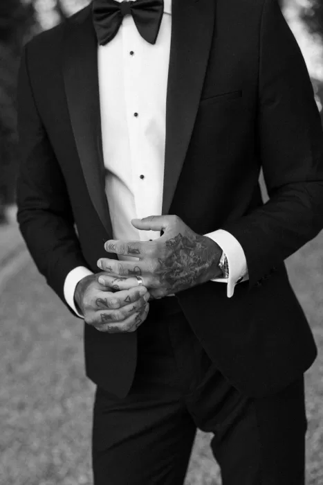 Black-and-white shot of the groom adjusting his cufflinks, showing tattoos and sharp tailoring.