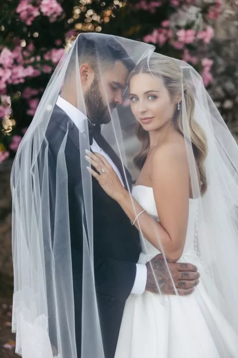 Romantic close-up of the bride and groom under the veil with pink florals in the background at Borgo Stomenanno.