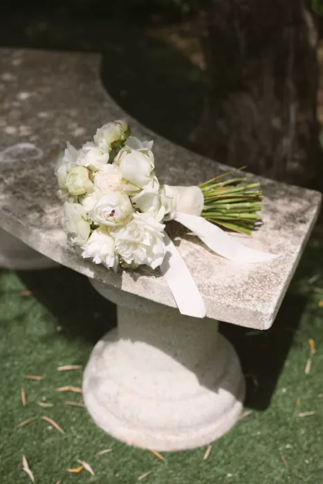 A delicate white peony bridal bouquet rests on a stone bench in the gardens of Cigarral de la Mercedes.