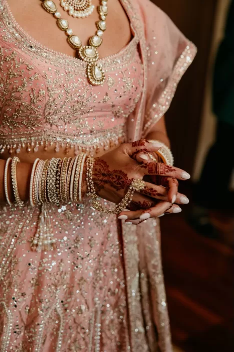 Close-up of bride’s hands adorned with bangles and henna, wearing a blush pink embroidered lehenga.