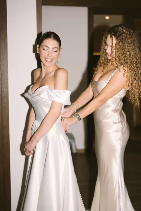 The bride smiles joyfully as her bridesmaid helps her with her gown inside Cigarral de la Mercedes.
