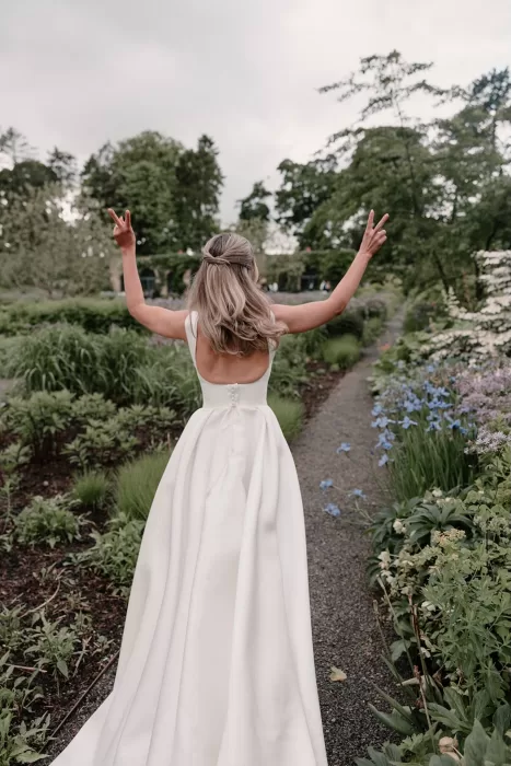 Bride raising her hands in joy while walking the garden paths of Middleton Lodge.