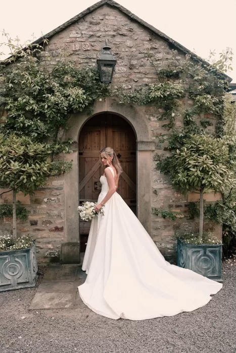 Bride posing elegantly in front of a rustic stone building at Middleton Lodge.