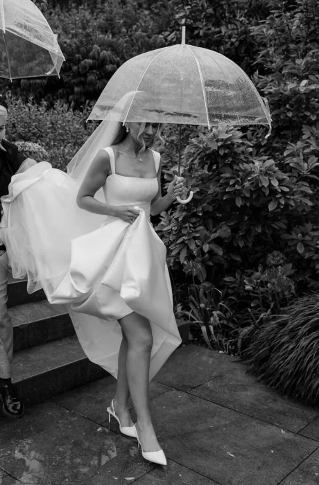 Bride walking with umbrella in the gardens of Middleton Lodge on a rainy wedding day.