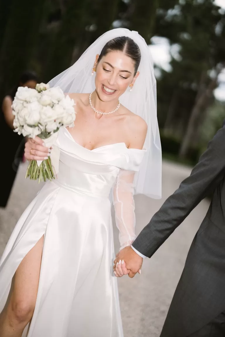 The bride smiles joyfully while holding her bouquet, walking hand in hand with her groom at Cigarral de la Mercedes.