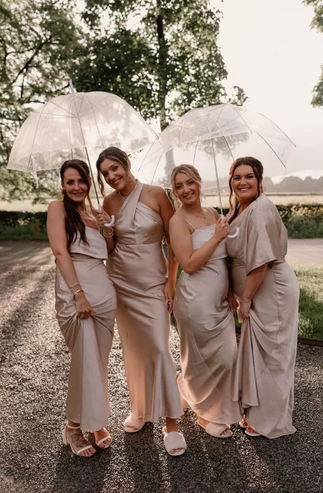 Bridesmaids in satin dresses holding clear umbrellas at Middleton Lodge.