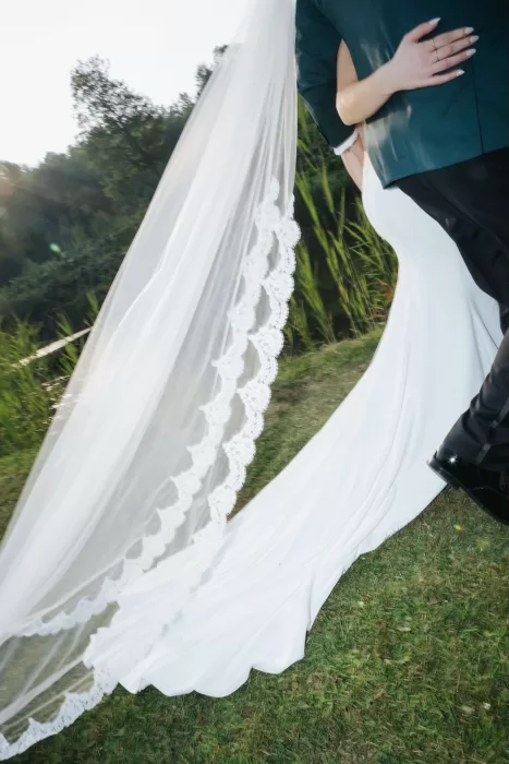 Bride and groom embrace by the water at Château Ste. Agnès, her lace-edged veil flowing dramatically in the evening sun.