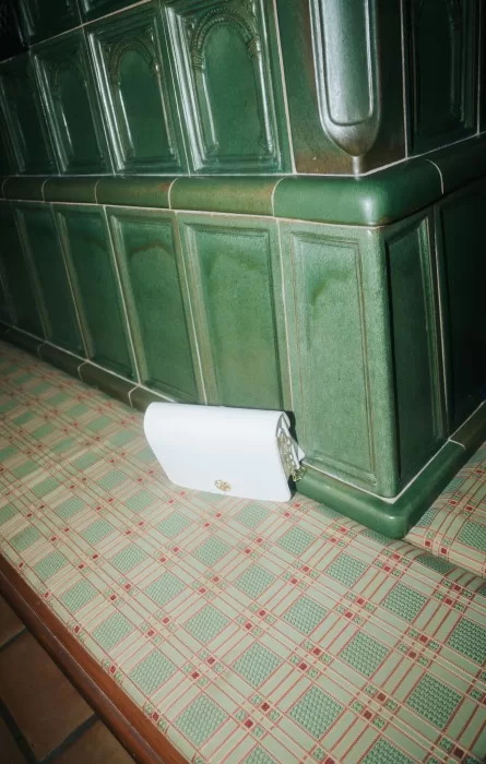 White clutch resting on patterned seating beside an ornate green-tiled stove inside Château Ste. Agnès.