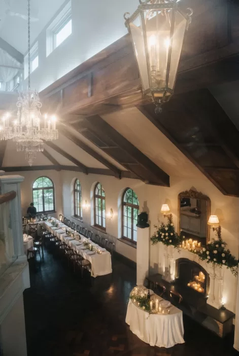Elegant indoor reception setup at Château Ste. Agnès with long tables, chandeliers, and a floral-covered fireplace.