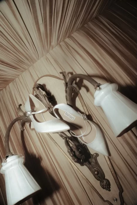 Pair of satin bridal heels resting atop a vintage wall sconce at Château Ste. Agnès, lit with soft warm light.