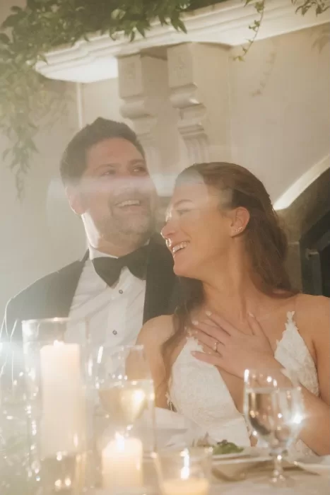 Bride and groom laughing during reception speeches, surrounded by candlelight and joy at Château Ste. Agnès.
