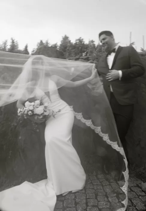 Bride’s dramatic veil flowing in the breeze as a guest helps adjust it outside Château Ste. Agnès.