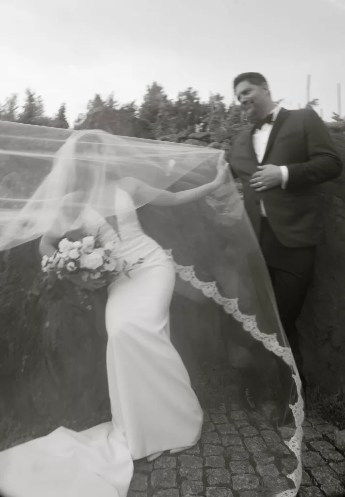 Artistic black-and-white shot of bride and groom at Château Ste. Agnès with her veil floating in the wind, capturing movement and joy.