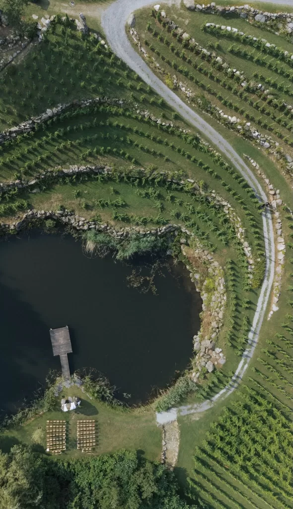 Aerial view of terraced vineyards and lakeside ceremony setup at Château Ste. Agnès, surrounded by lush greenery and curved stone paths.