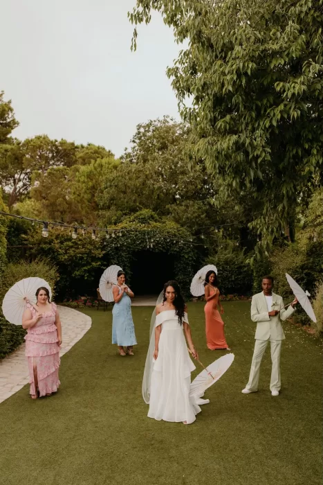 Bride with wedding party holding white parasols in the gardens of Cigarral de las Mercedes.