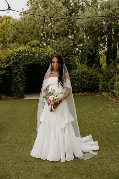 Bride in flowing gown with long veil standing under string lights at Cigarral de las Mercedes.