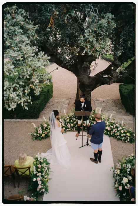 Wedding ceremony beneath a large tree surrounded by flowers at Cigarral de las Mercedes.