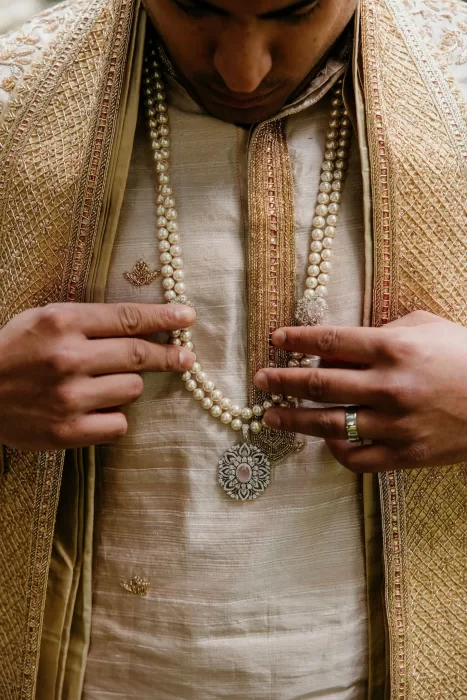 Close-up of the groom adjusting his pearl necklace and sherwani at Cigarral de las Mercedes.
