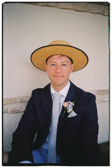 Groom in navy suit with straw hat smiling at Cigarral de las Mercedes.