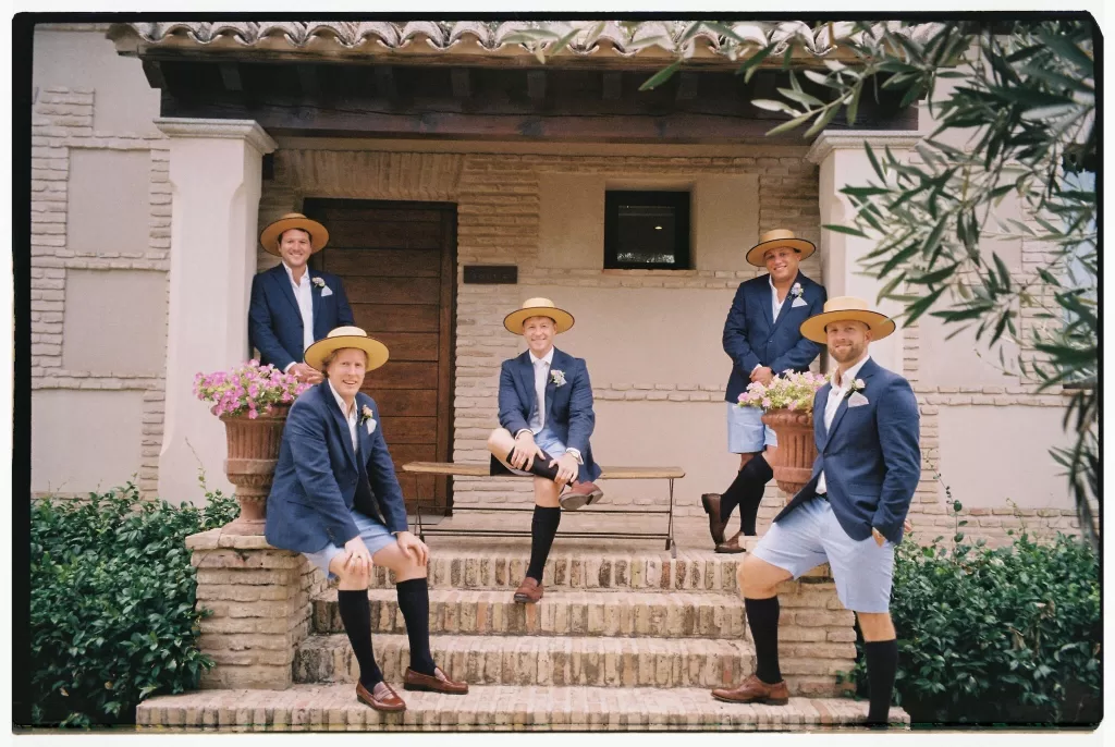 Groomsmen in navy blazers and straw hats posing on stone steps at Cigarral de las Mercedes.