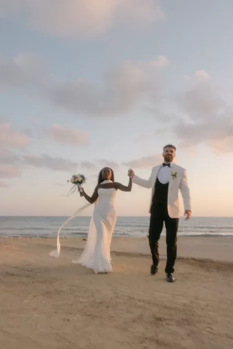 Bride and groom holding hands and walking joyfully along the sandy beach at Coral Residences.