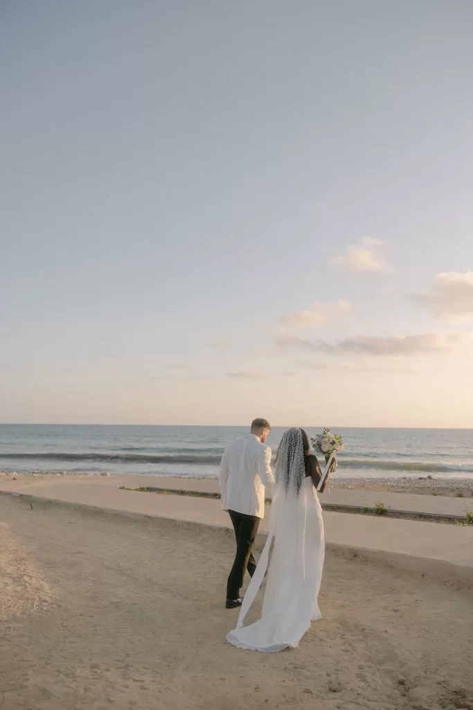 Bride and groom walking along the sandy beach at Coral Residences under a soft golden sunset.