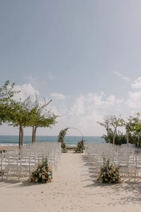 Elegant seaside ceremony setup with floral arch and white chairs at Coral Residences.