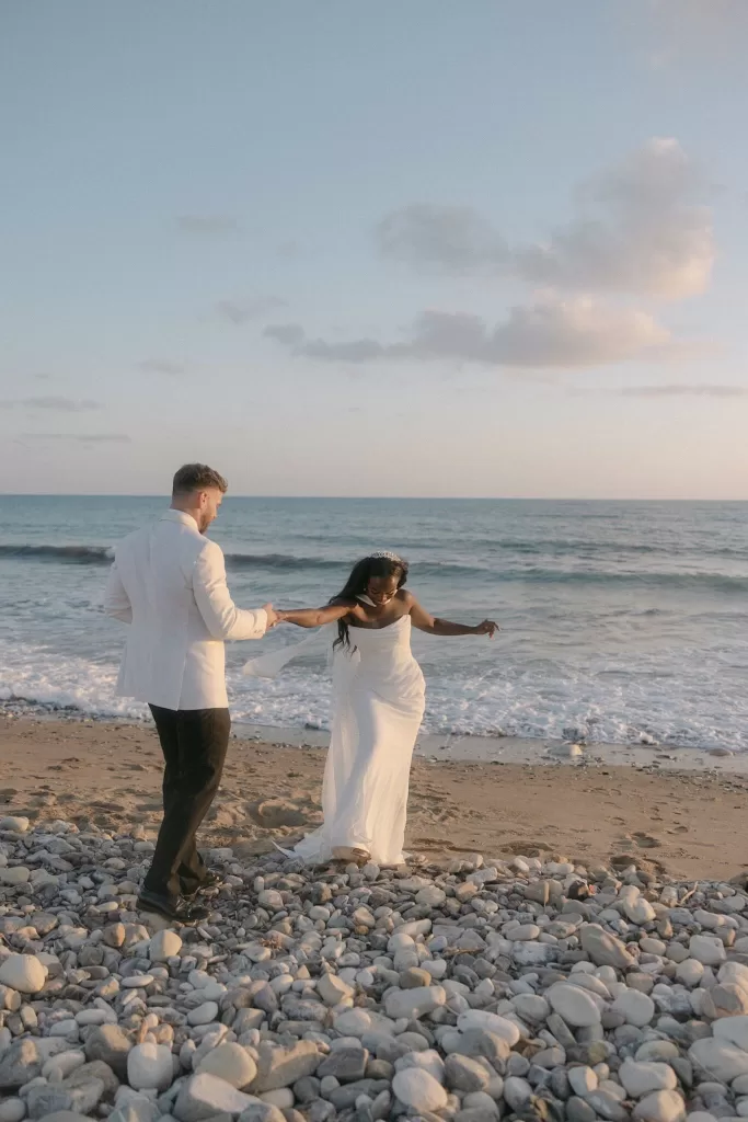 Groom leading bride along the pebbled shoreline at Coral Residences.