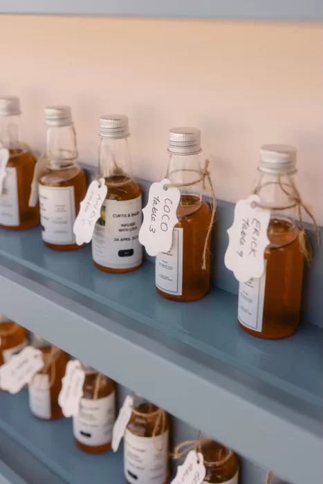 Small glass bottles of amber liquid with handwritten guest name tags at Coral Residences wedding.