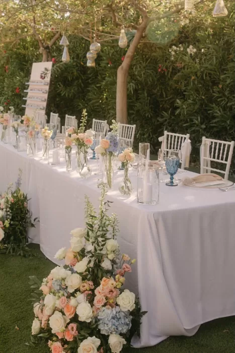 Long white-clothed head table decorated with pastel flowers and blue glassware at Coral Residences.