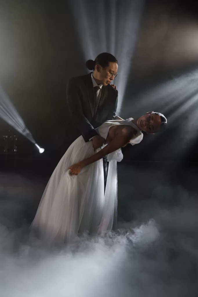 Groom dipping bride during their first dance, surrounded by stage lighting and low-lying fog.