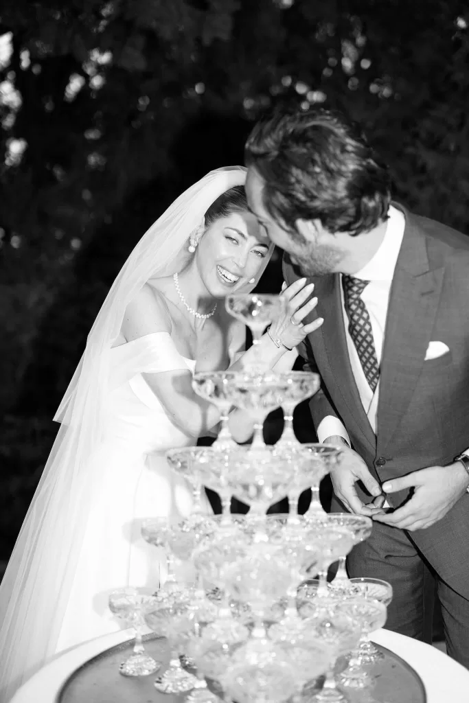 Bride and groom laugh joyfully while pouring champagne at their Cigarral de la Mercedes wedding reception.