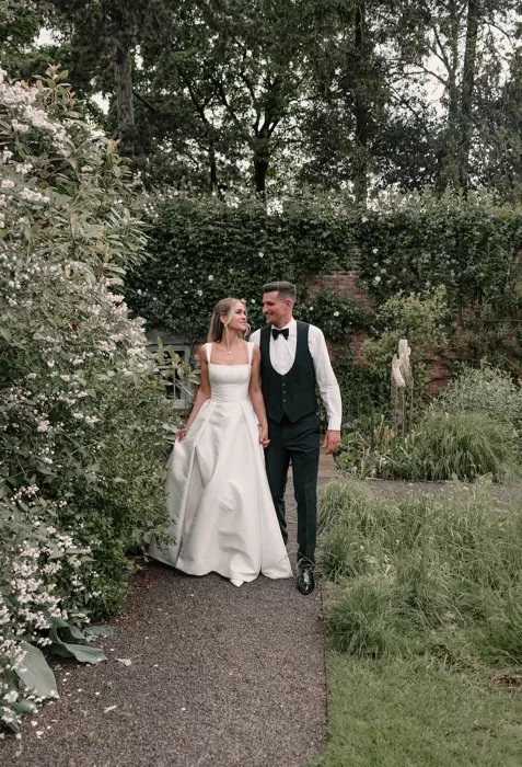 Bride and groom walking hand in hand through the romantic gardens at Middleton Lodge.