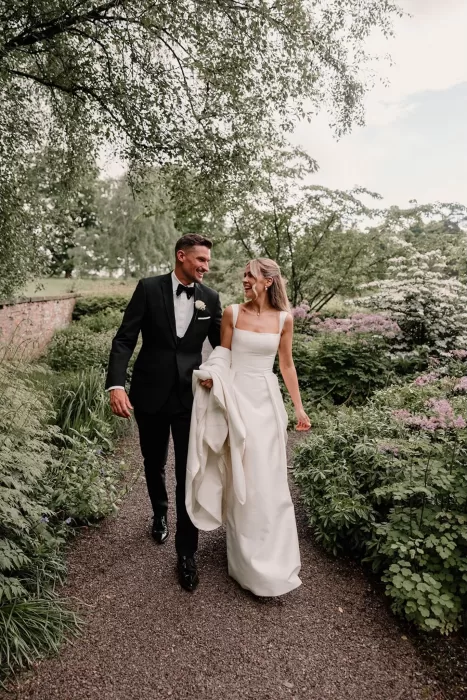 Bride and groom smiling while walking together along garden paths at Middleton Lodge.